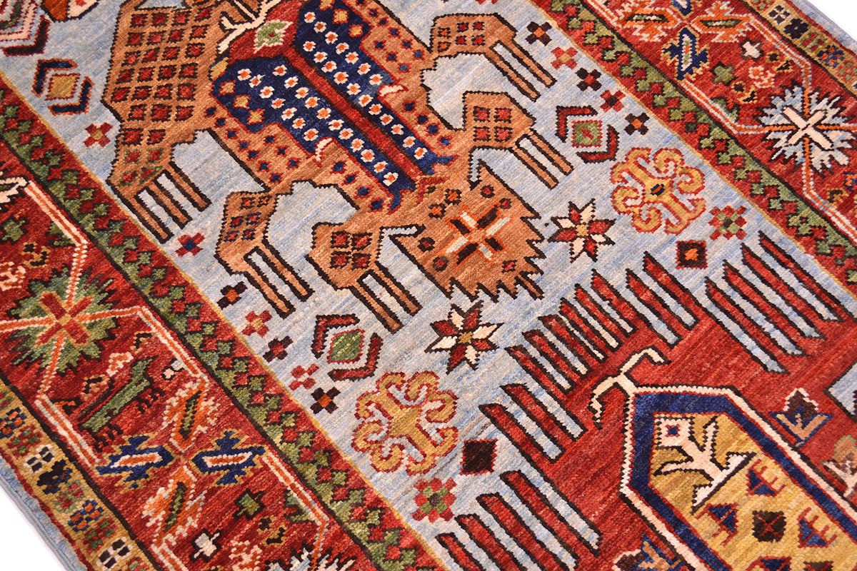 A close-up of a traditional patterned antique style Afghan runner with geometric and animal motifs in red, orange, blue, beige, and green on a light gray field.