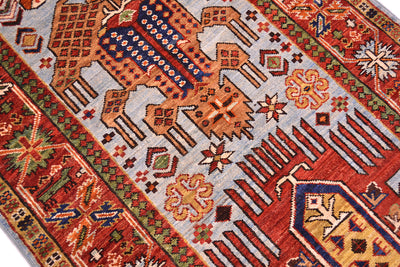 A close-up of a traditional patterned antique style Afghan runner with geometric and animal motifs in red, orange, blue, beige, and green on a light gray field.