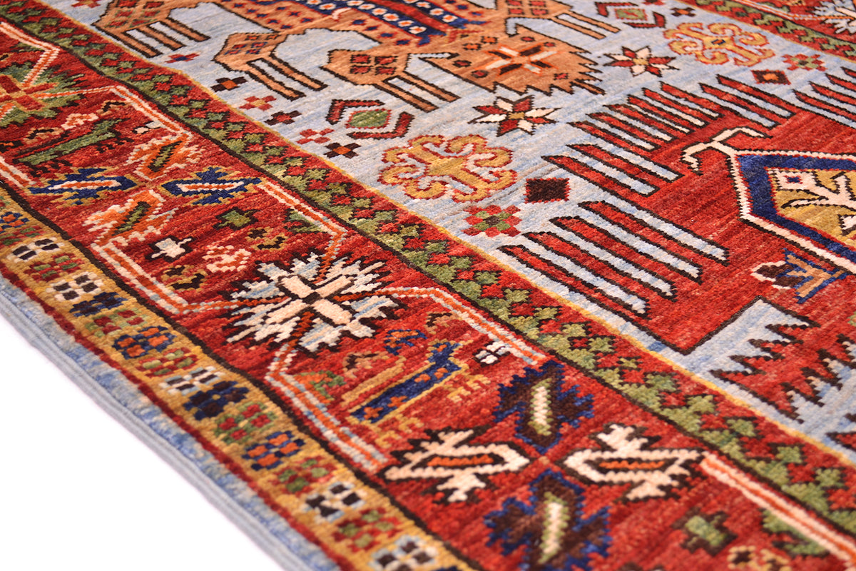 A close-up of a traditional handwoven Taimani runner from Afghanistan with a complex geometric pattern in red, orange, blue, green, and beige, shown on a white background.