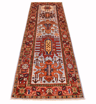 A long rectangular antique looking tribal Afghan runner rug with an intricate geometric and floral pattern, featuring a central field and detailed borders in red, orange, beige, blue, and green, shown flat against a white background.