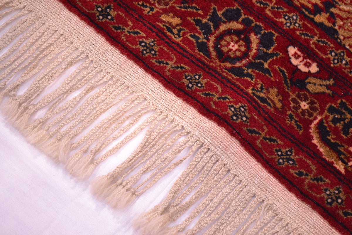 Old Belouch-Tavusi rug corner fringe close-up with red border and textured pale tassels.