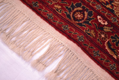 Old Belouch-Tavusi rug corner fringe close-up with red border and textured pale tassels.