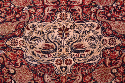 Old Belouch-Tavusi rug close-up of central cream medallion on red patterned background.