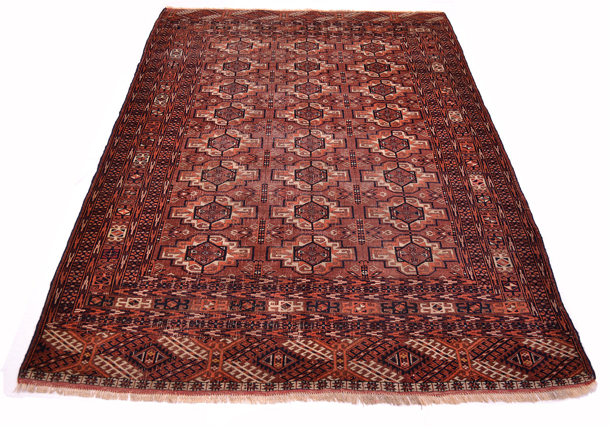 A traditional Turkoman Tekke antique wool rug with a geometric pattern in shades of brown, orange, beige, and black, shown flat against a white background.