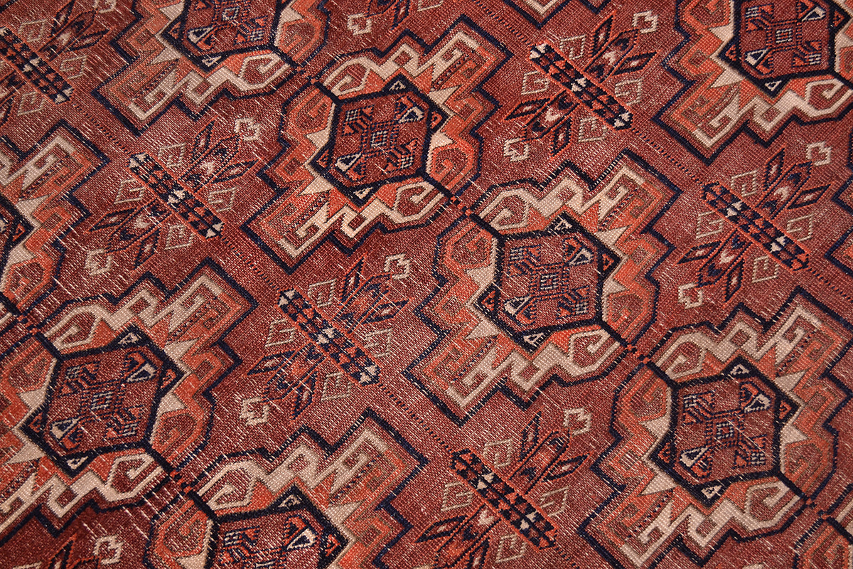 A close-up of a patterned fine antique Tekke rug with a geometric design in  brown-terracotta, orange, beige, and black.