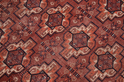 A close-up of a patterned fine antique Tekke rug with a geometric design in  brown-terracotta, orange, beige, and black.