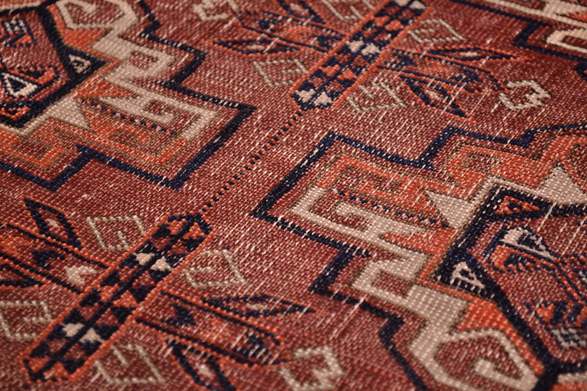 Close-up of a worn antique Tekke rug with a geometric pattern in terracotta-brown, beige, orange and dark navy blue.