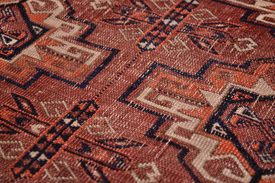 Close-up of a worn antique Tekke rug with a geometric pattern in terracotta-brown, beige, orange and dark navy blue.