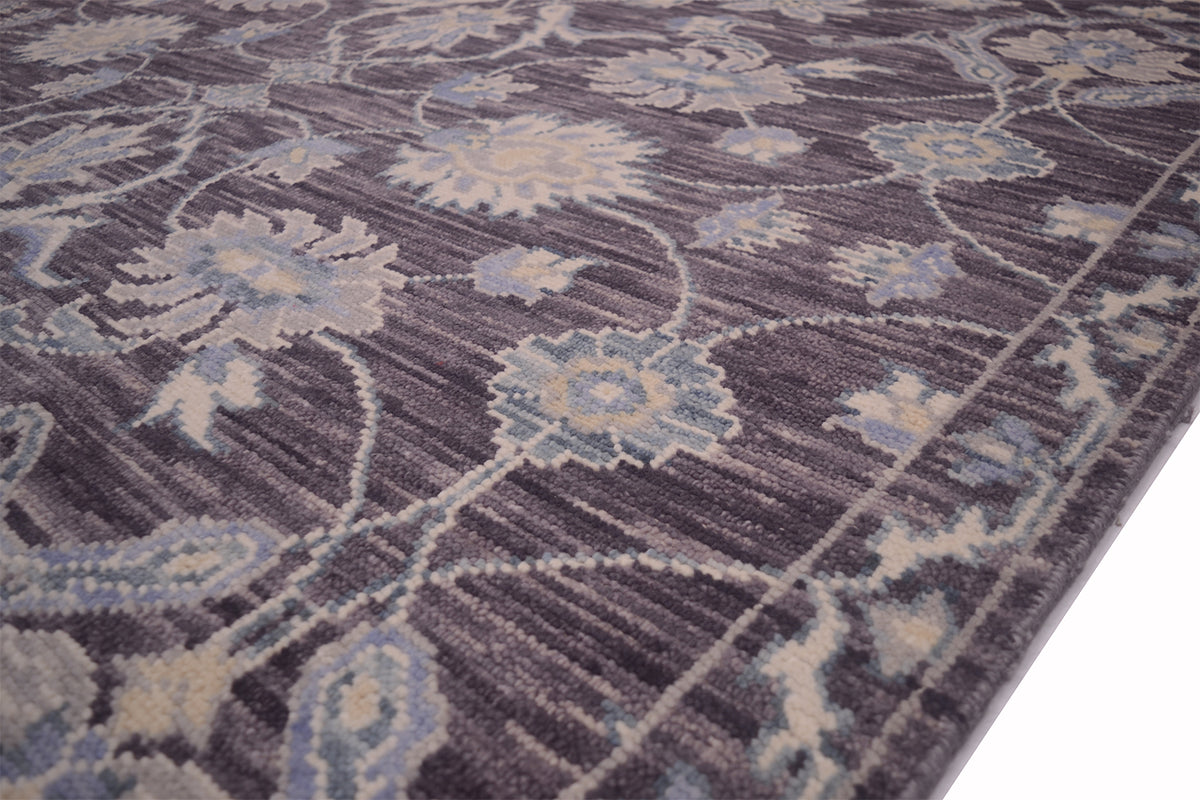 A close-up of a patterned Tonal rug with a floral and vine design in muted blue, beige, and gray tones on a pewter background.