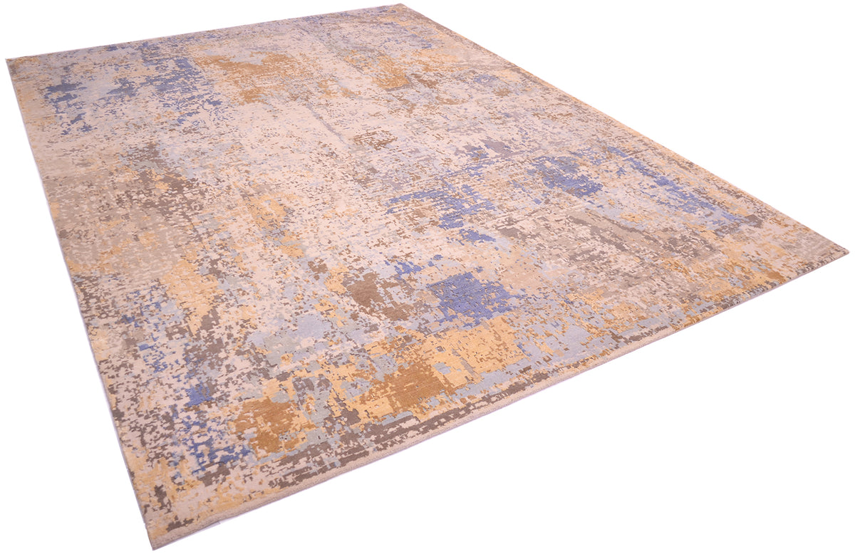 Angled view of handmade Indian carpet with a variety of soft colours and textures. Raised pure silk handcut area of light golden silk with sky blue and light blue.  Dark bronze and beige tones of the main matte areas of wool pile.