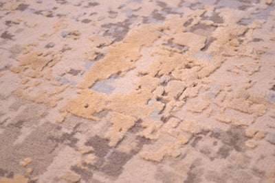 Detailed view of handknotted carpet with soft greys and beiges wool pile with raised silk highlights of golden creams and abstract textures and high low pile.