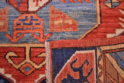 Close-up of a patterned rug showing a rust red field with orange, and beige geometric motifs and a white fringe edge.