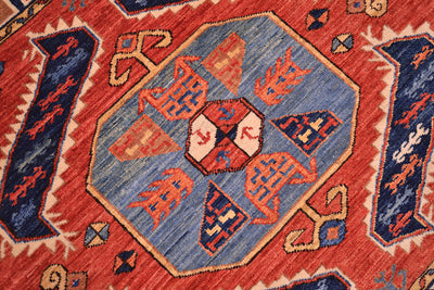 Close-up of a woven rug showing a central blue hexagonal medallion with rust, orange, and cream geometric motifs, surrounded by a rust field and dark blue corner motifs.