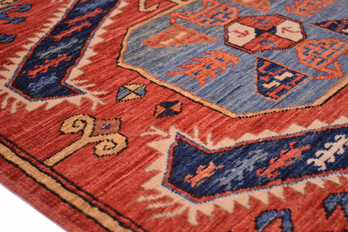 Close-up of a patterned Afghan area rug with a rust red field, blue geometric motifs, and beige accents.