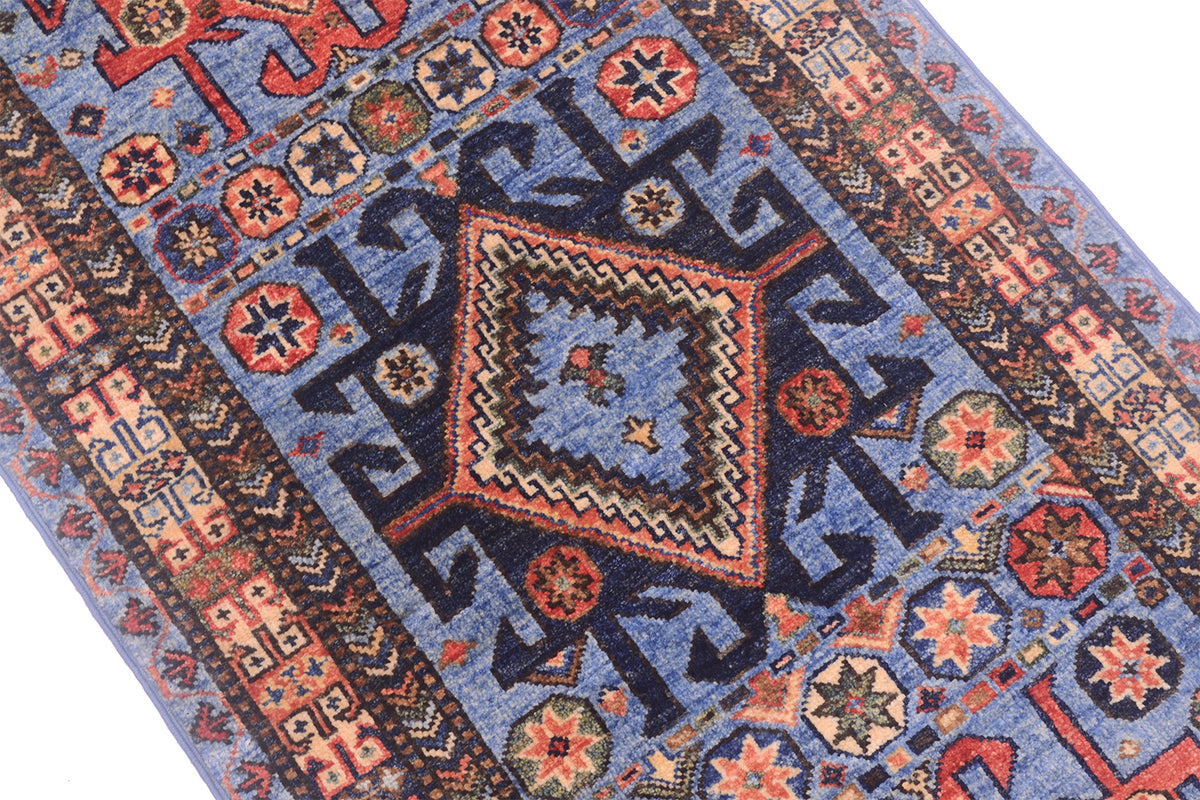 A close-up of a traditional patterned Turkmen runner with a blue field, featuring a central diamond medallion and geometric borders in navy, red, beige, and orange.