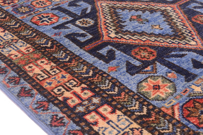 A close-up of a traditional patterned Afghan Turkmen runner with a blue field, dark navy borders, and geometric motifs in red, beige, and green.