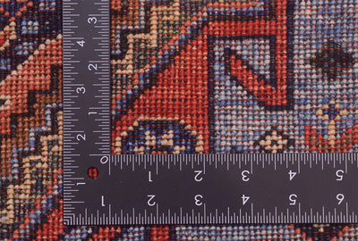 Close-up of the hand-knotted weave of a Turkmen tribal style runner patterned rug with a metal ruler placed along the edge to show scale of the knot density, featuring a geometric design in rust red, blue, beige, and black.