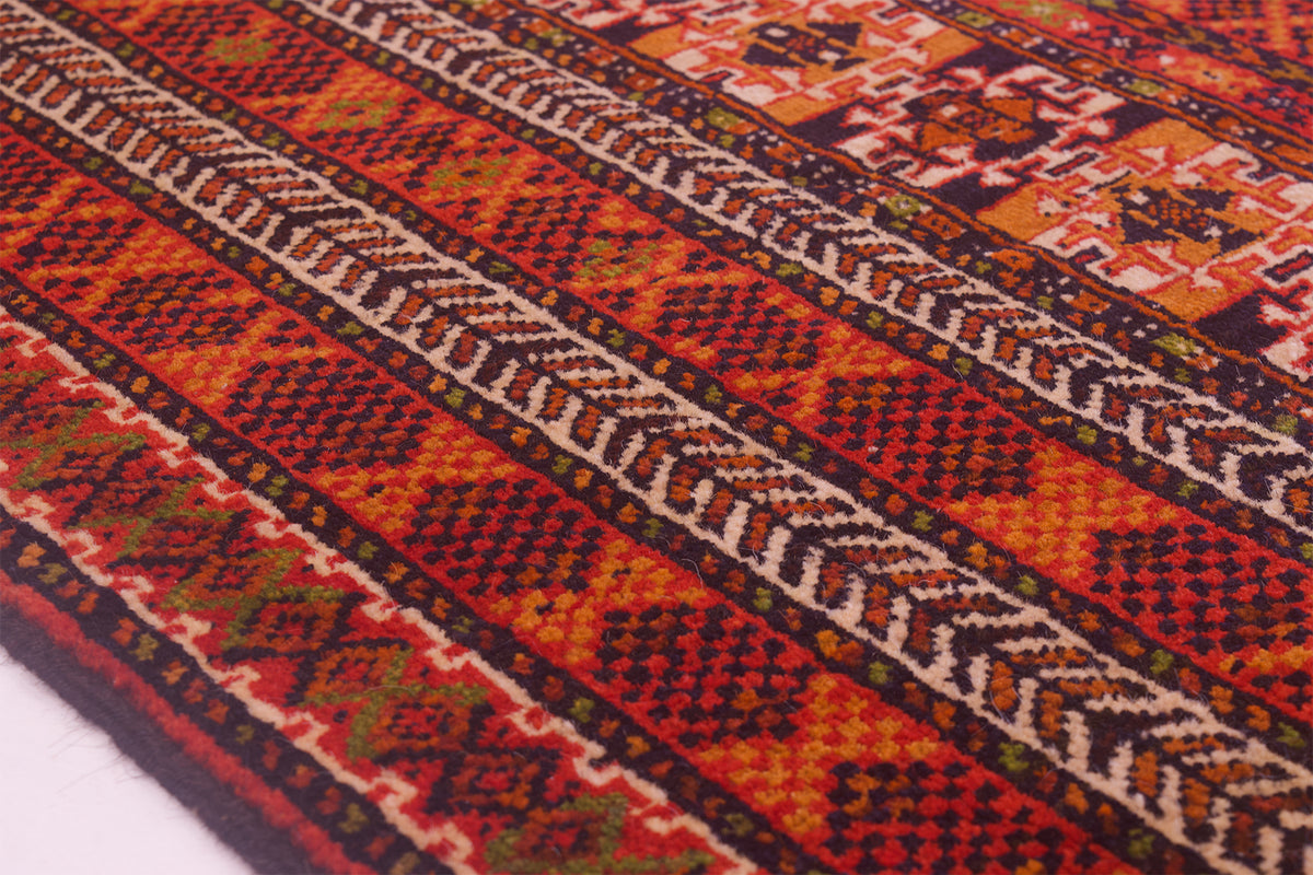 A close-up of a woven Turkoman Prayer rug with a bold geometric pattern in red, orange, black, and cream, showing detailed textile texture.