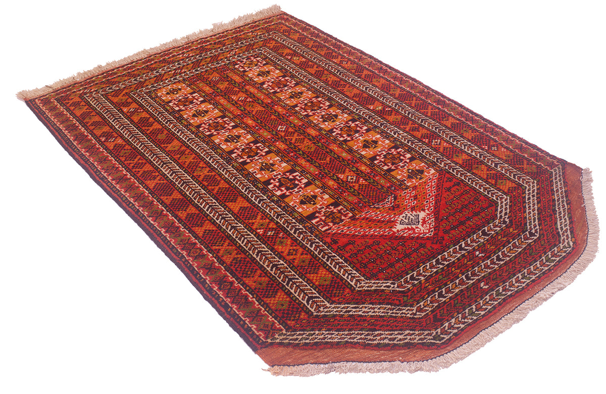 A traditional rectangular Oriental Prayer rug with a complex geometric and floral pattern in shades of red, orange, brown, and beige, featuring fringed edges on a white background.