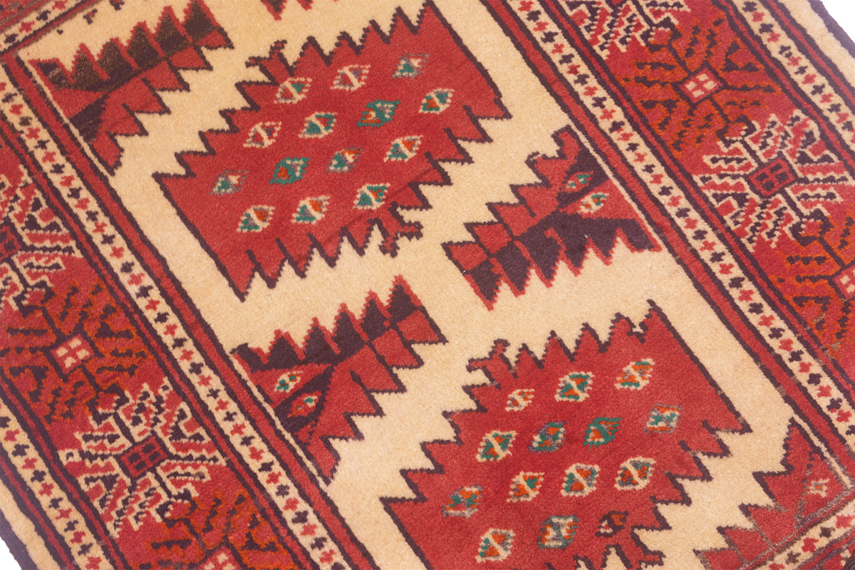 A close-up of a traditional geometric patterned rug mat with red central panels, beige borders, and dark brown and green accents.