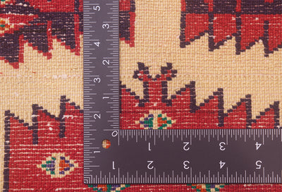 Close-up of a patterned rug mat with a dark gray metal ruler placed over it to show scale, featuring a red, beige, and dark brown geometric design.