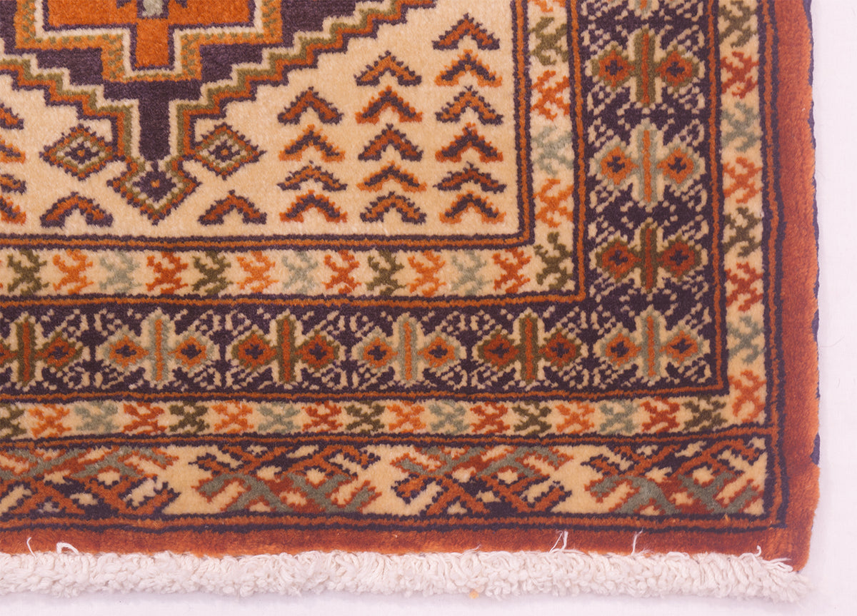 Close-up of a rug/mats corner showing cream, rust orange, navy, and muted green geometric motifs with a fringed edge.