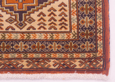Close-up of a rug/mats corner showing cream, rust orange, navy, and muted green geometric motifs with a fringed edge.