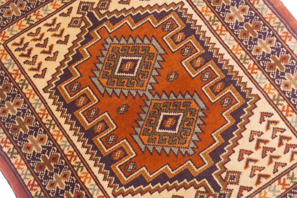 close-up of a traditional geometric patterned rug mat with a warm rust-orange center, cream borders, and dark brown and navy details.
