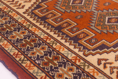 A close-up of a traditional rug mat showing its detailed woven design in orange, beige, brown, and dark blue.