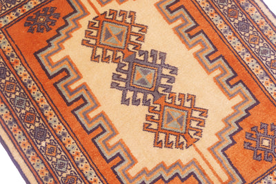 A close-up of a patterned rug with a cream center, orange field, and geometric motifs in blue, brown, and orange.