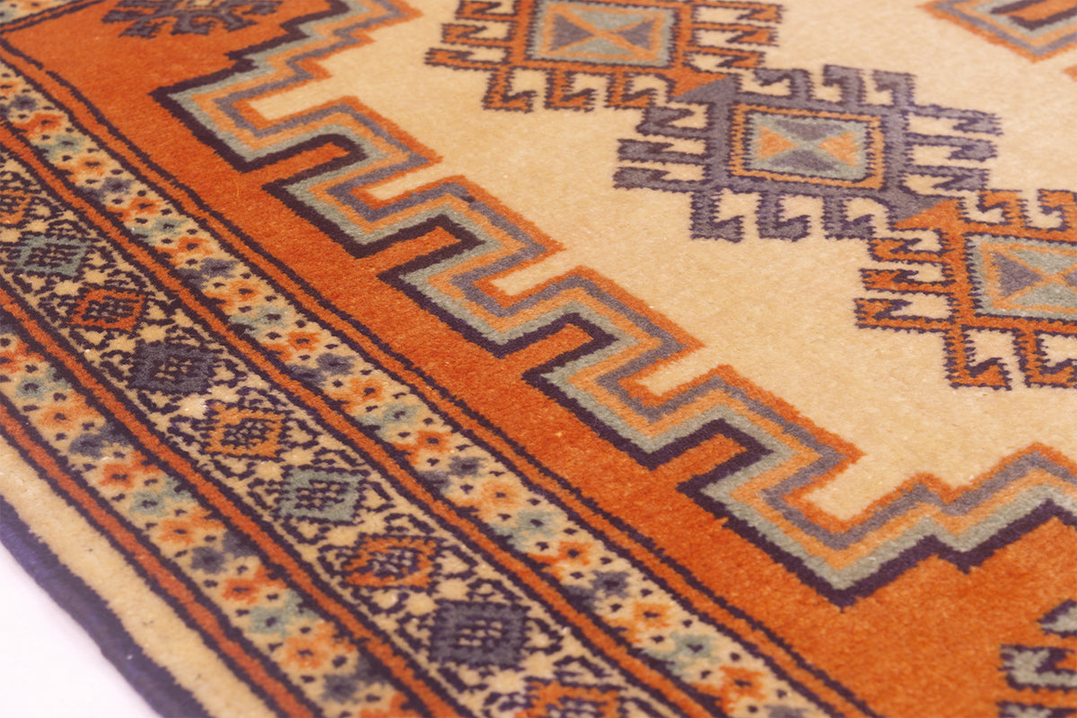 Close-up of a patterned area rug  mat with a warm orange and beige field, and geometric motifs in navy, gray, and orange.