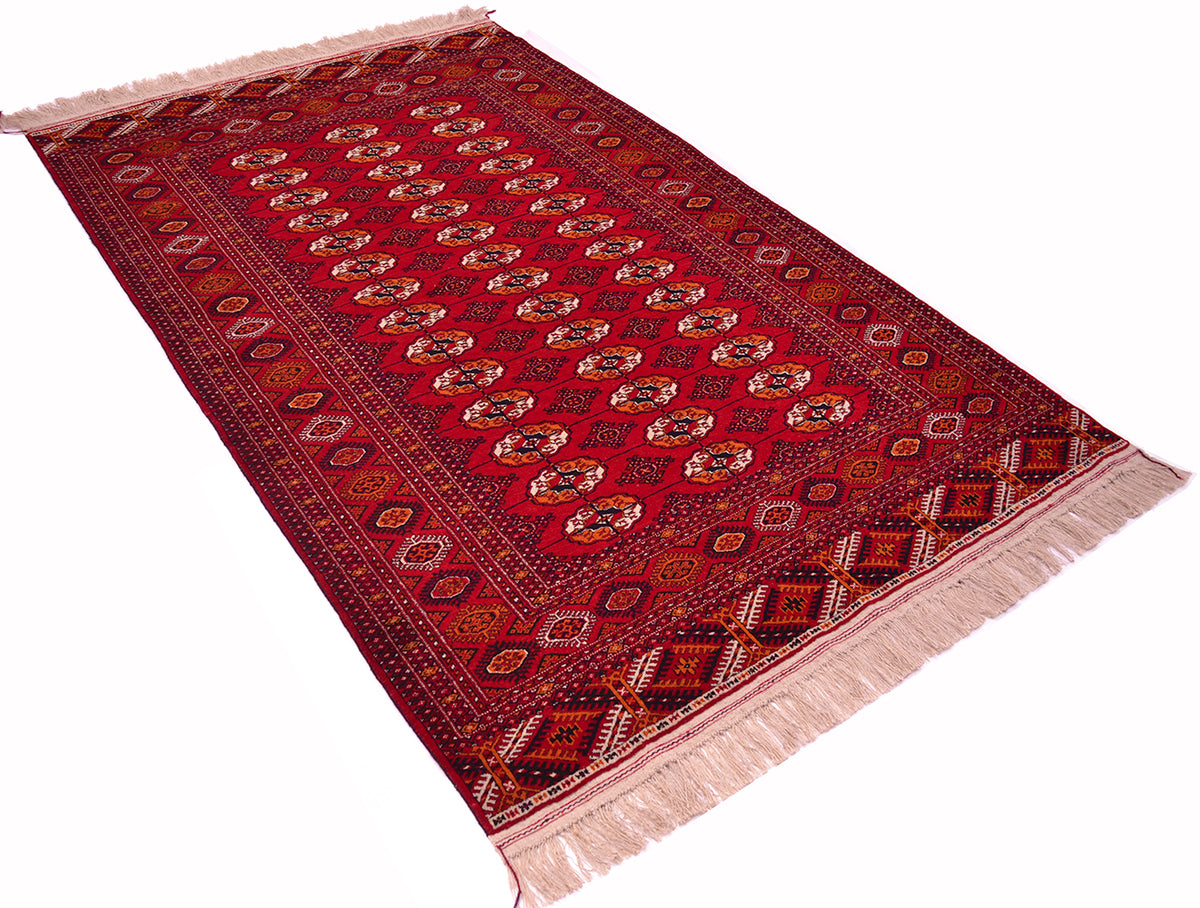 A traditional red Turkoman Bokhara rug with intricate geometric patterns and fringed ends, shown on a plain white background.