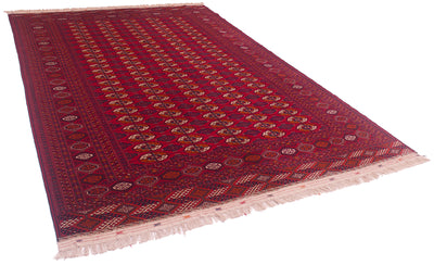 A traditional Bokhara-style Turkoman wool carpet with a deep red field, intricate geometric and floral patterns in navy, beige, and gold, and cream-coloured fringe on the ends.