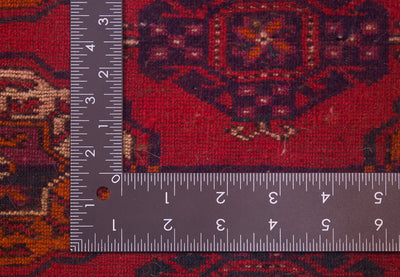 A close-up of the hand-knotted weave of a red Turkoman Bokhara Carpet with a dark L-shaped metal ruler placed along the corner to show the scale of the knotting.