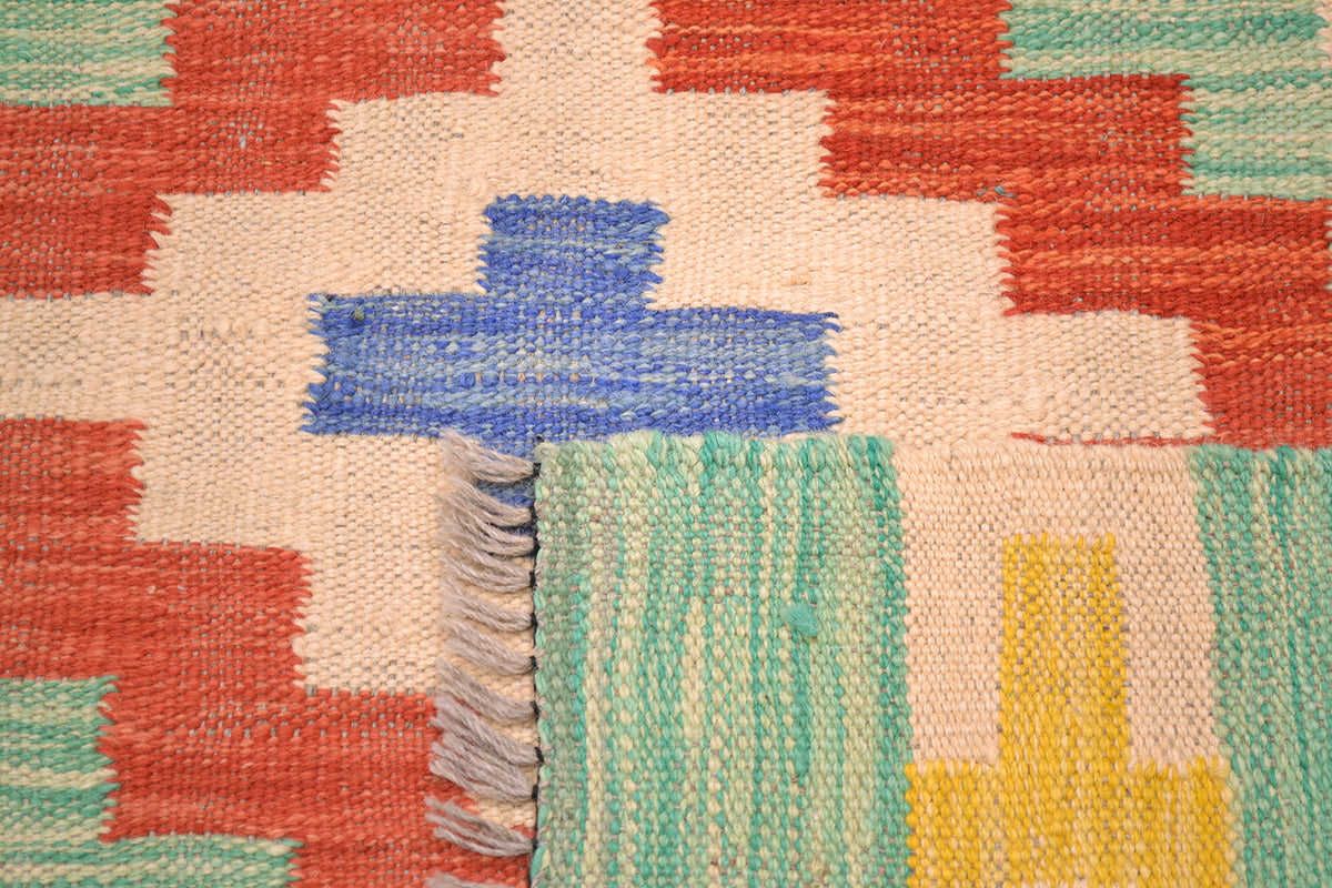 Handwoven kilim rug corner close-up with blue cross over green and orange blocks