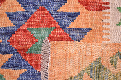 Close-up of the underside corner of a woven handwoven multicolour Kilim long runner rug showing a geometric pattern with orange, blue, red, green, and beige sections, including a fringed edge.