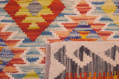 Close-up of a handwoven geometric multicolour Afghan Kilim rug with a cream base and bold red, orange, yellow, blue, and grey patterns, showing the texture and corner detail.