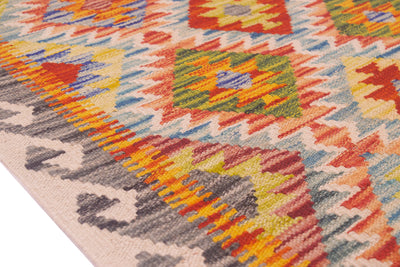 Close-up of a Afghan handwoven Kilim rug with a geometric multicolour pattern in orange, yellow, green, blue, red, cream and grey on a white base.