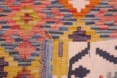 Close-up of a handwoven Afghan Multicolour Kilim Rug showing a colourful geometric pattern with pink, yellow, blue, orange, and cream tones, including a fringed edge and part of a dark abstract motif.