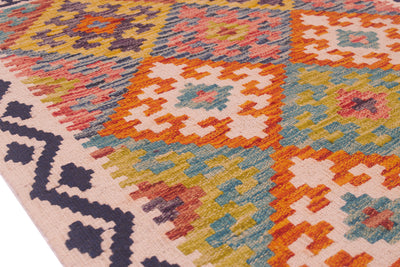 A close-up of a handwoven Kilim rug with a colourful geometric pattern in orange, pink, blue, yellow, and cream, featuring a dark navy patterned border on a white background.
