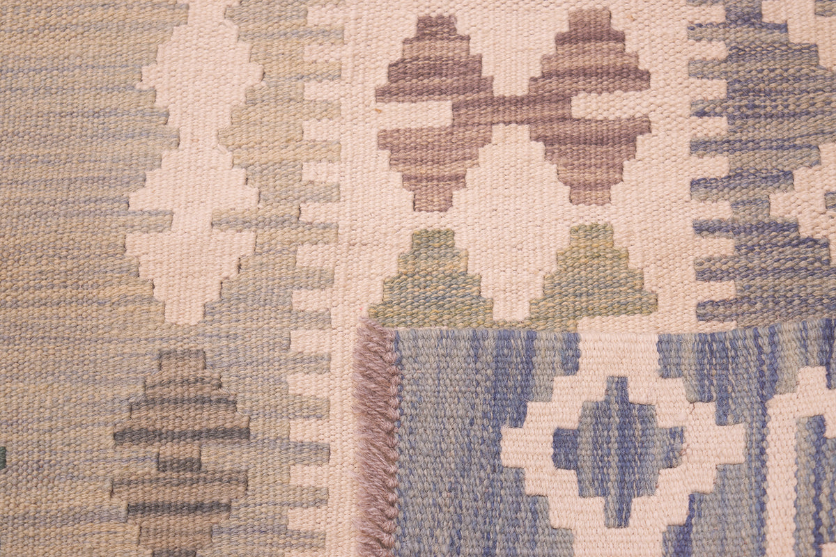 Close-up of a handwoven Afghan Kilim rug with a geometric pattern in beige, dusty blue, and muted green.