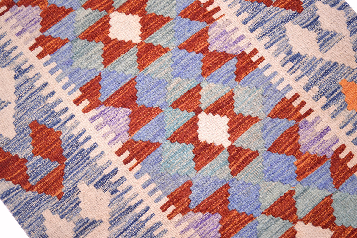A close-up of short Afghan Kilim runner with a geometric pattern in rust red, dusty blue, lavender purple, and cream.