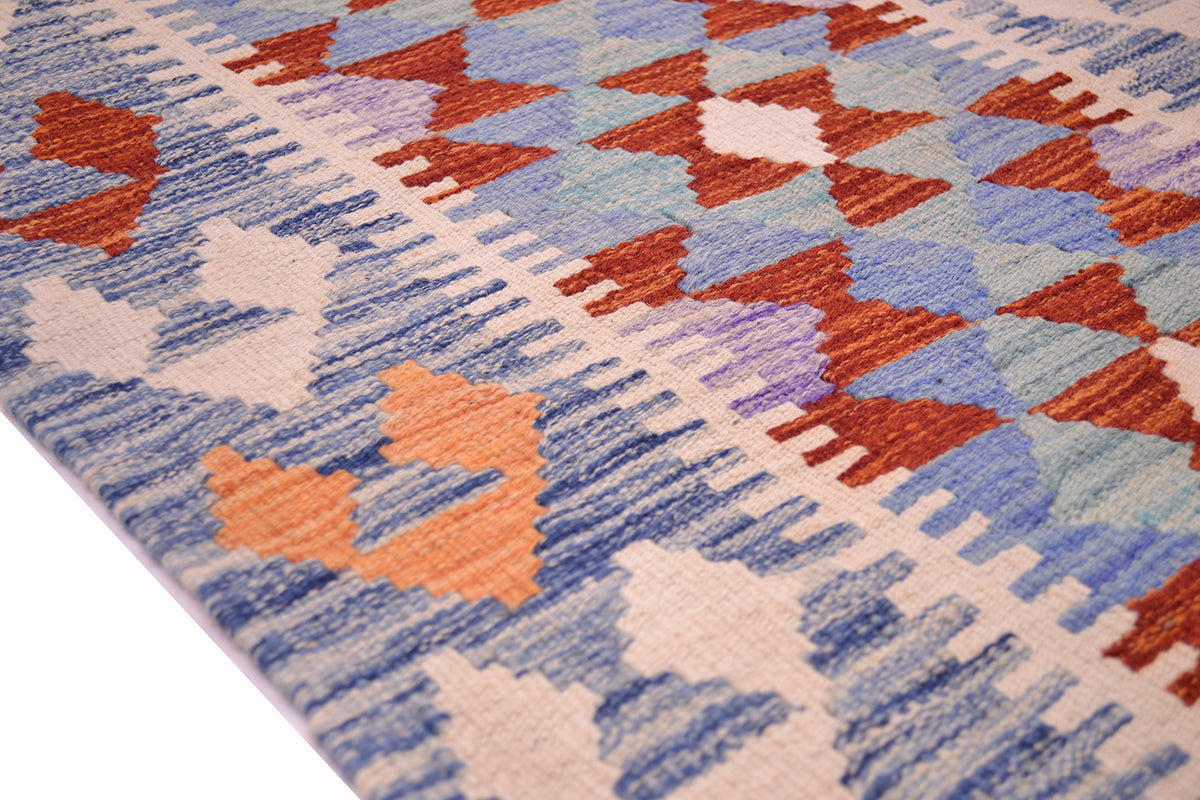 A close-up of a border of a handwoven Kilim short runner with a geometric pattern in blue, rust red, peach, and cream.