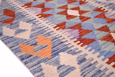 A close-up of a border of a handwoven Kilim short runner with a geometric pattern in blue, rust red, peach, and cream.