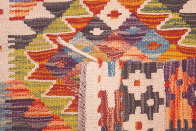 Close-up of the weave of a handwoven geometric Afghan Kilim strip/rug with a multicolour pattern including orange, red, blue, green, yellow, purple, and cream, featuring a white fringed edge.