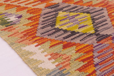 Close-up of a handwoven Afghan Kilim strip / rug corner showing a geometric pattern with orange, yellow, purple, grey, beige, and cream tones.