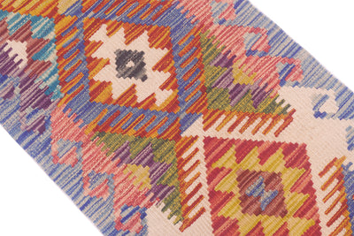 A close-up of a colourful handwoven small Kilim strip with a geometric diamond pattern in pink, orange, yellow, blue, green, and purple on a light cream background.