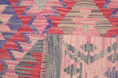 Close-up of the weave of a handewoven Kilim rug showing a geometric pattern in pink, red, blue, and grey with a fringed edge.
