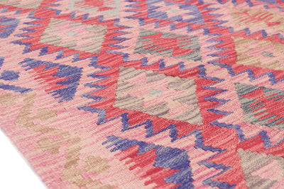 A close-up of a woven Afghan Kilim rug with a geometric pattern in pink, red, blue, beige, and grey.