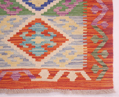 A close-up of a multicolour Kilim short runner rug showing its geometric pattern and fringed edge. The design features a central diamond motif in orange, light blue, and cream, surrounded by bands of orange, purple, green, and cream.